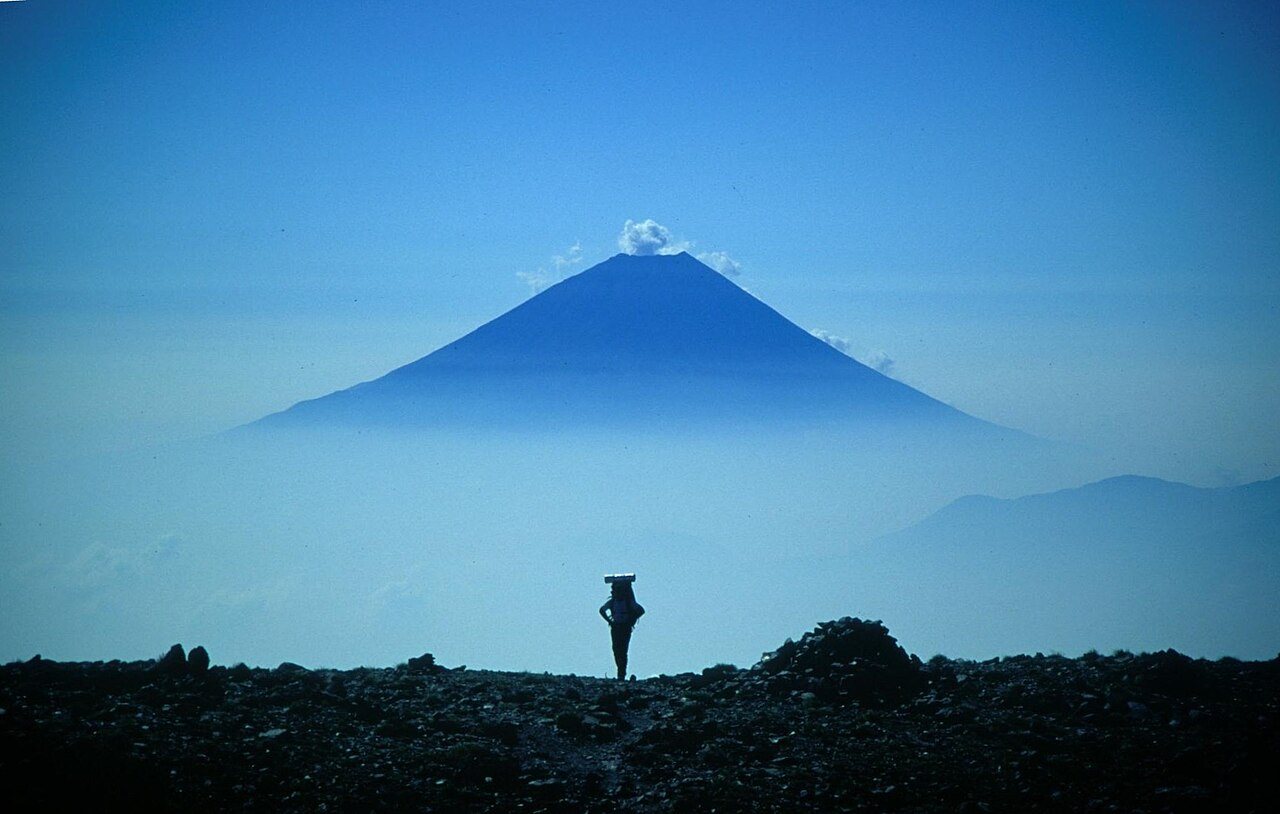 山頂に雲がかかる富士山とその手前に立つ登山者1人のシルエット