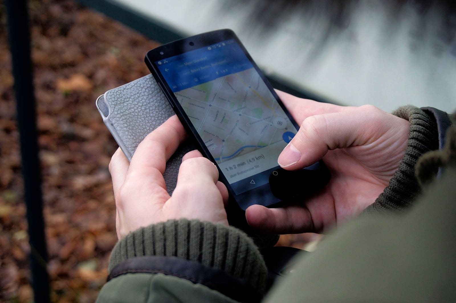 屋外で両手にスマホと財布を持ち地図アプリを操作する写真