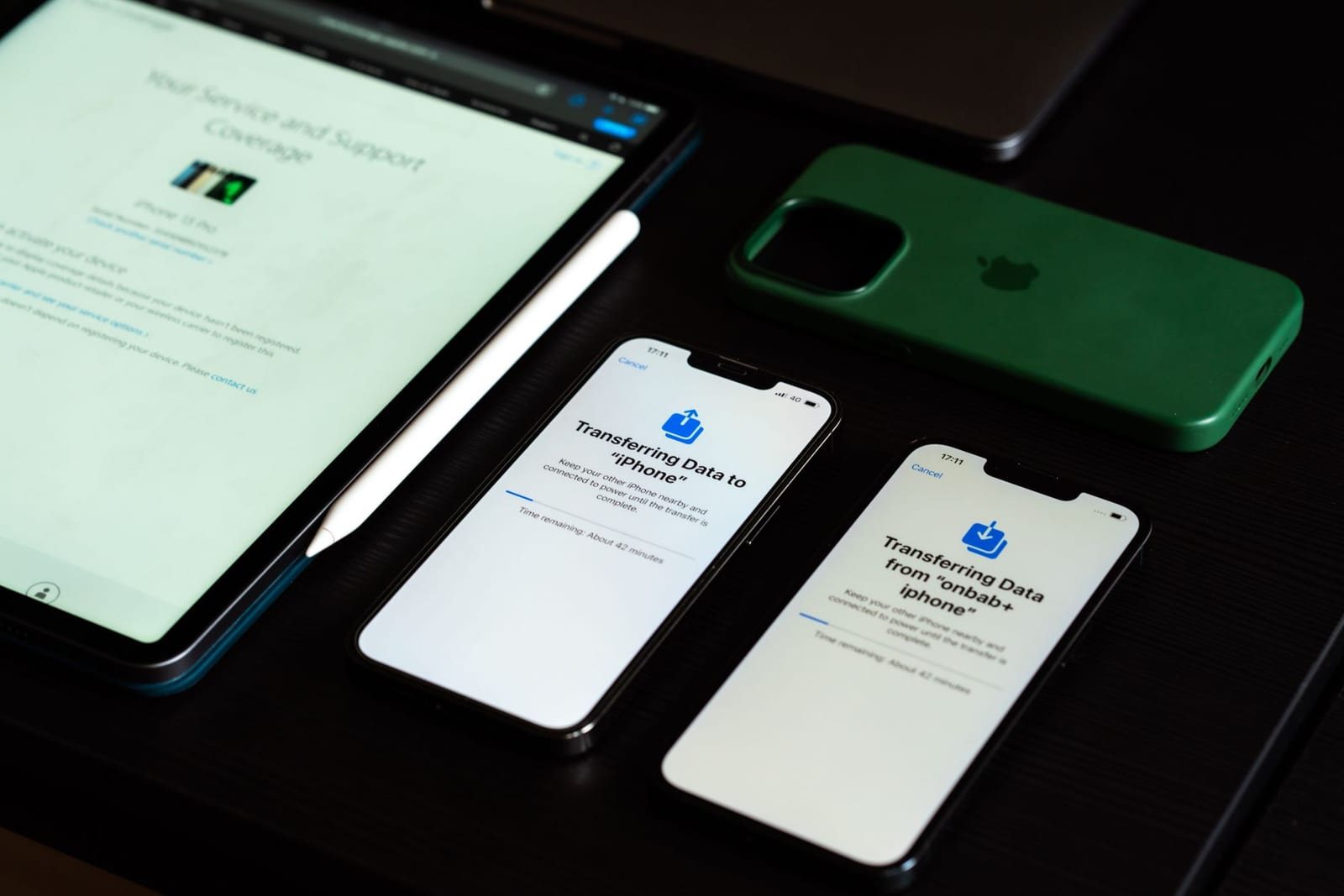 暗い机の上でデータ転送画面を表示した2台のスマホとタブレットが並んでいる