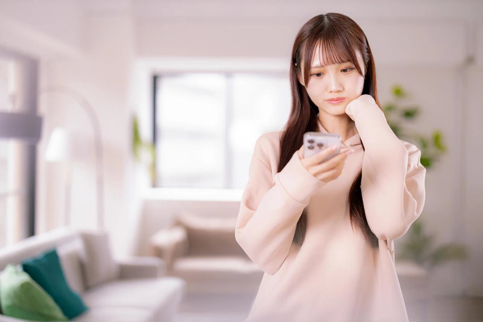 室内でスマートフォンを見つめる若い女性1人の写真