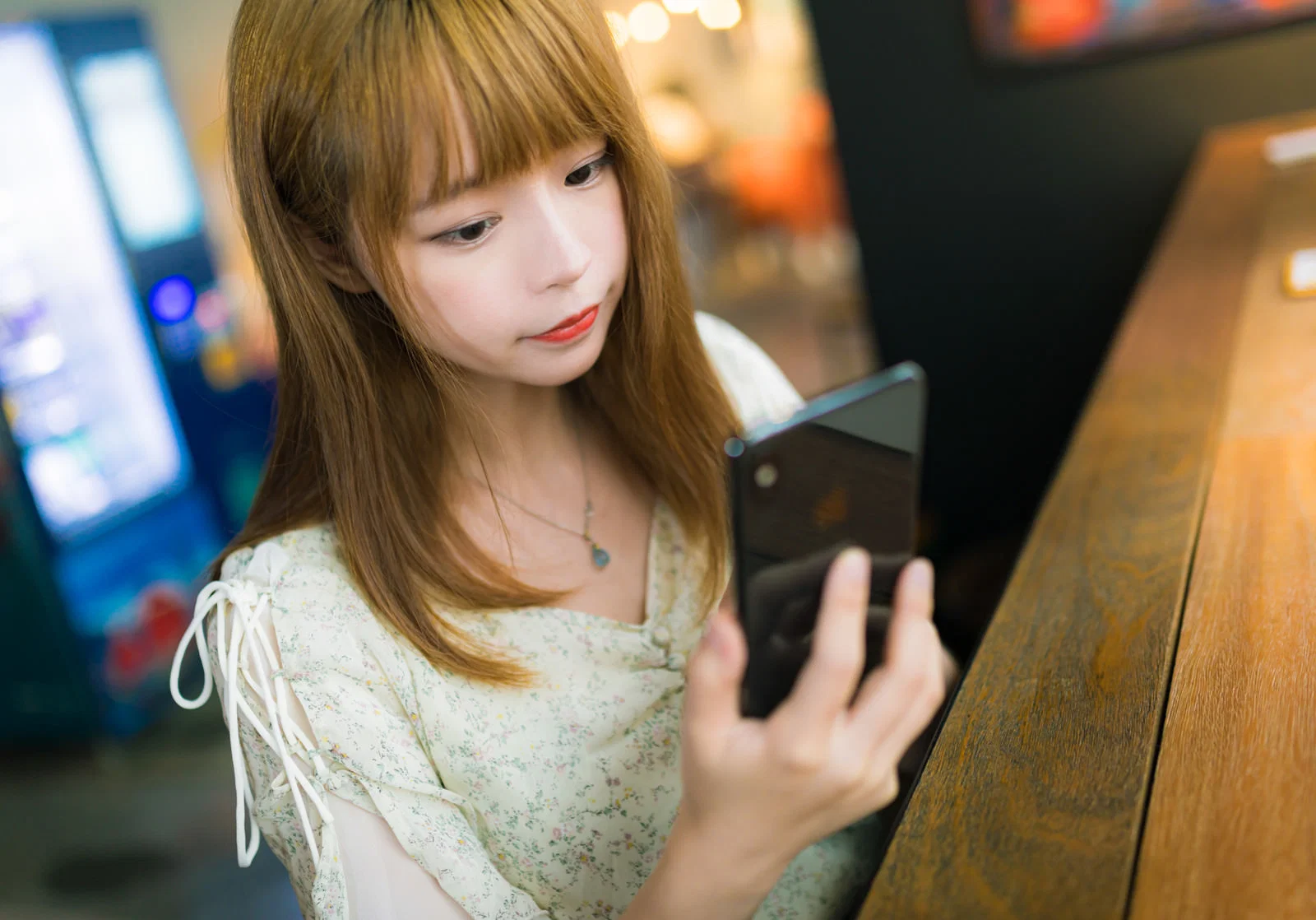 屋内で自動販売機を背に若い女性がスマートフォンの画面を一人で見ている