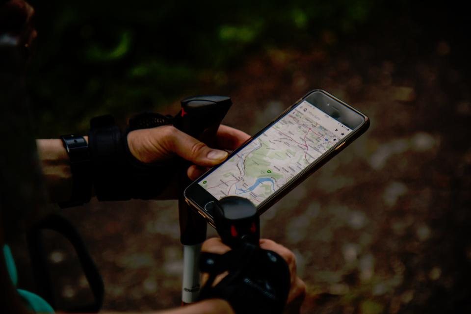 屋外で、登山用ポールを持つ人がスマートフォンの地図画面を確認している様子