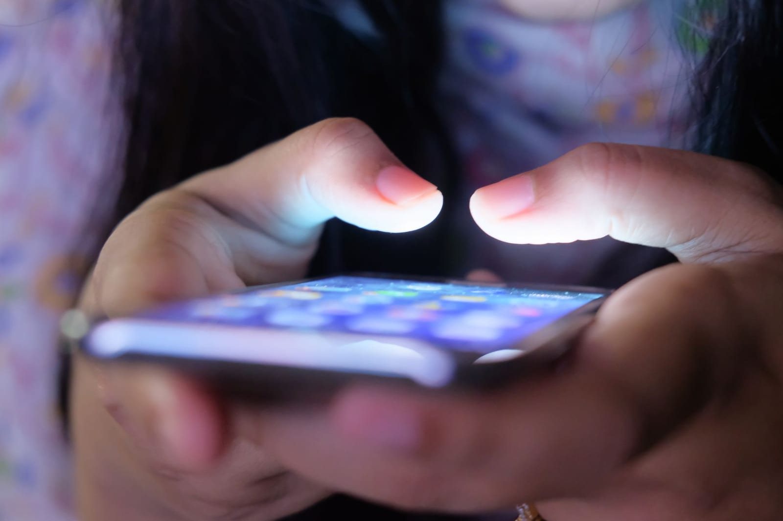 薄暗い室内で両手でスマートフォンを操作する人の指先のアップ