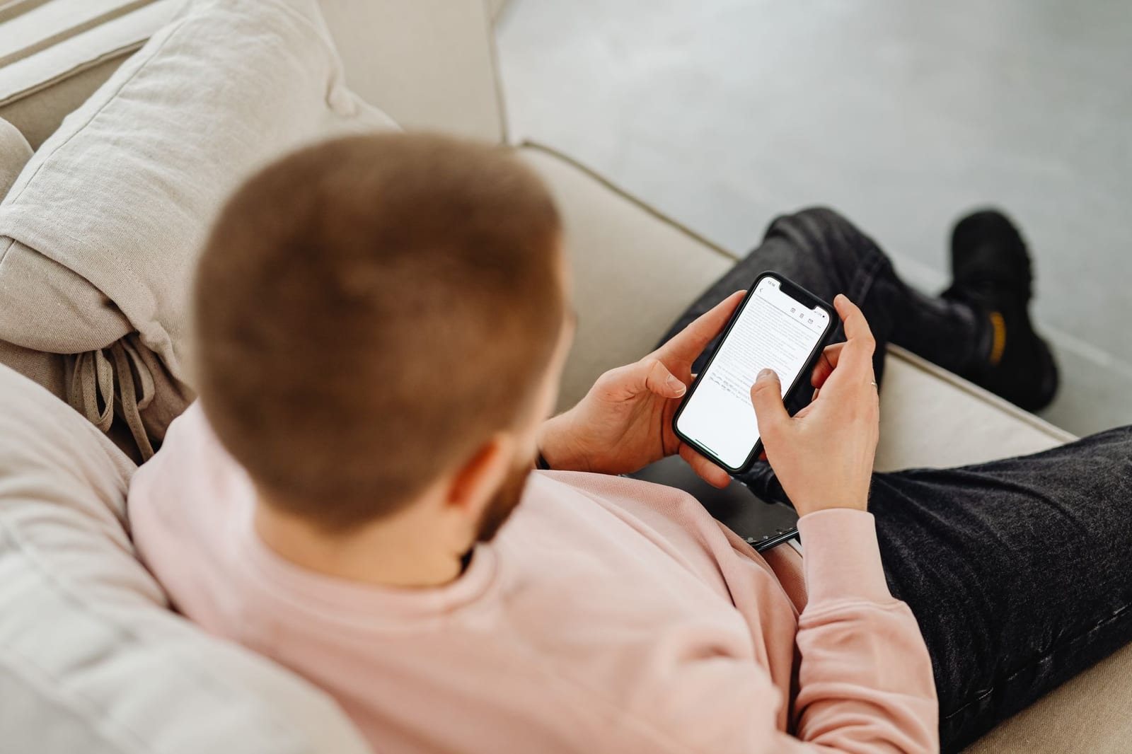 室内のソファに座り、スマートフォンを両手で操作する男性