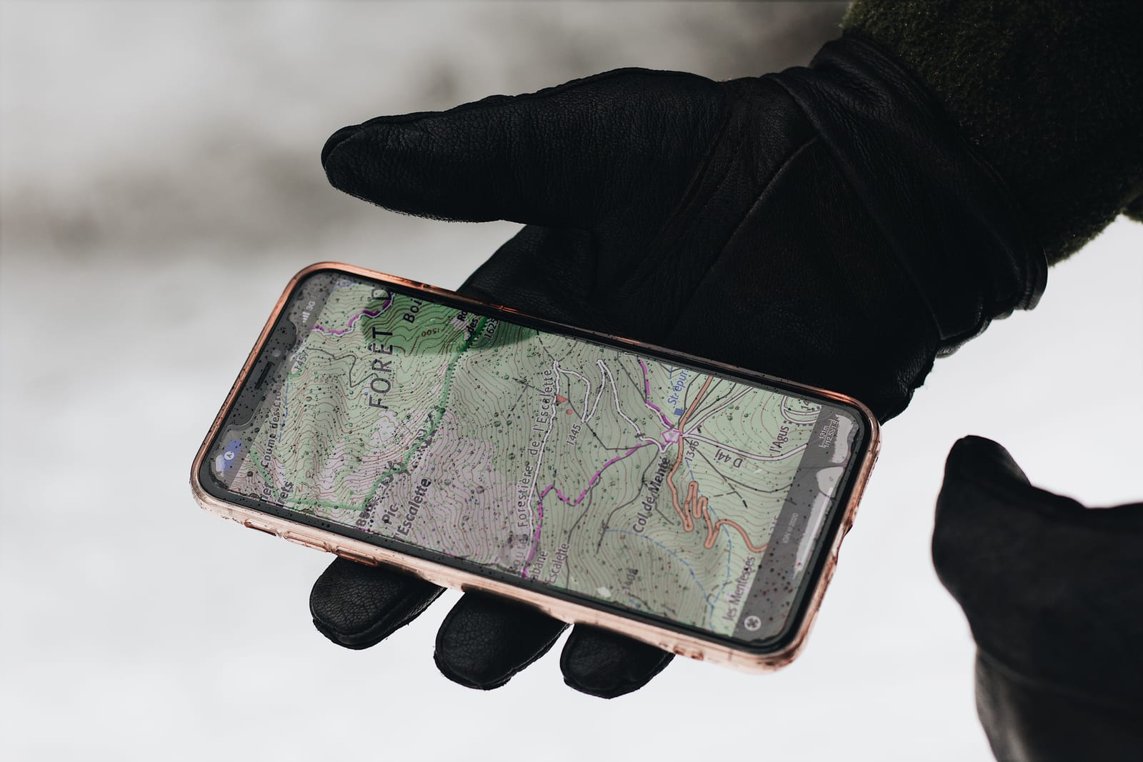 雪の屋外で黒い手袋をした手がスマートフォンの地図画面を持っている写真