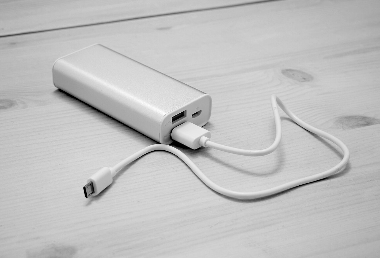 木製テーブルの上に置かれた白いモバイルバッテリーと2本の充電ケーブル(モノクロ写真)