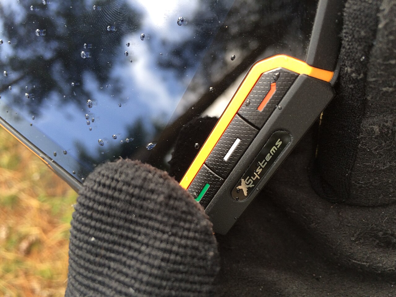 屋外で手袋をした手が水滴の付いた頑丈なスマートフォンを持つ接写