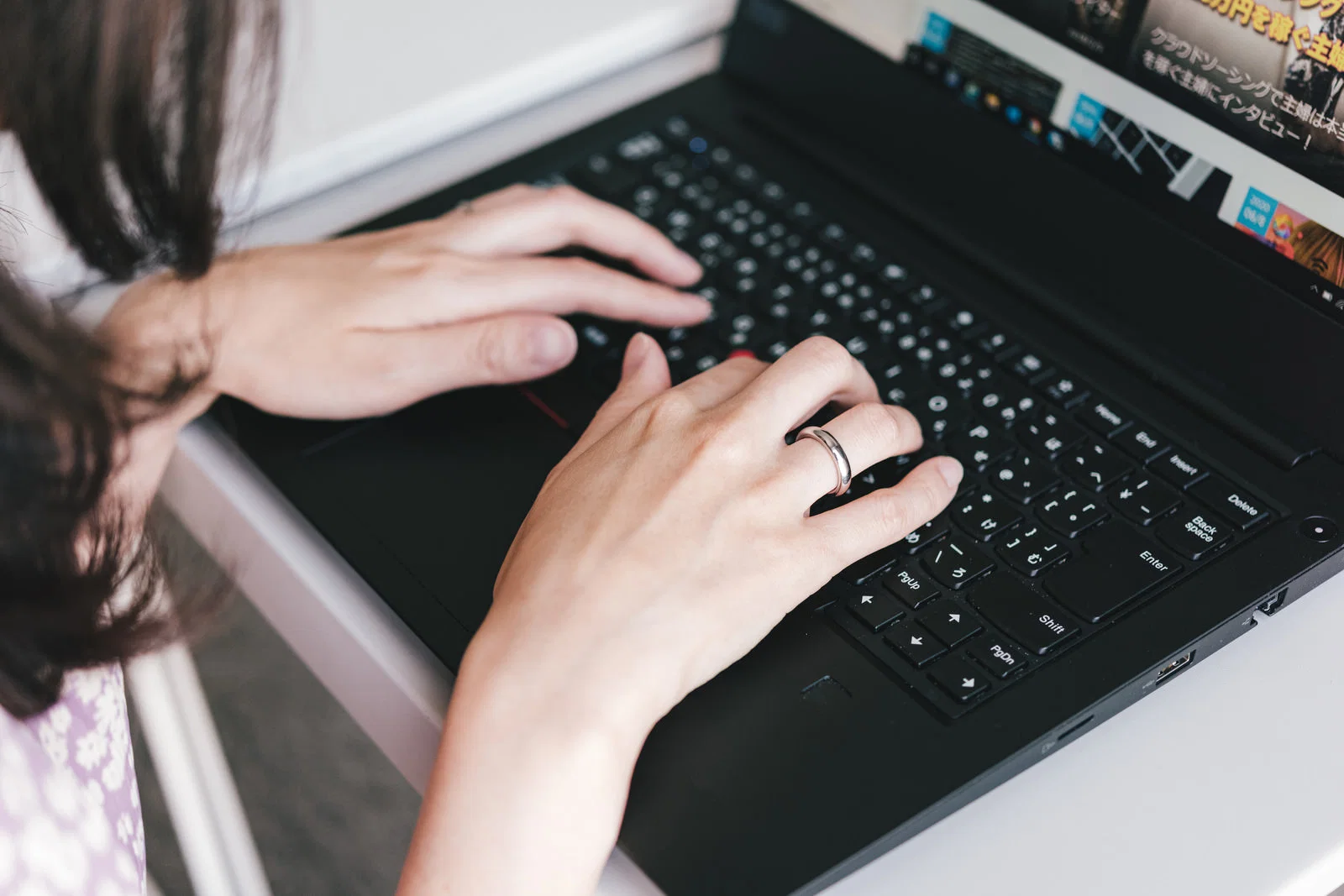 黒いノートPCのキーボードを両手で操作する人物を上から写した写真